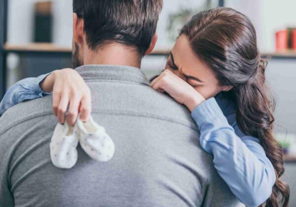 Woman-crying-hugging-man-and-holding-baby-socks-a-2021-08-30-01-45-16-utc-scaled