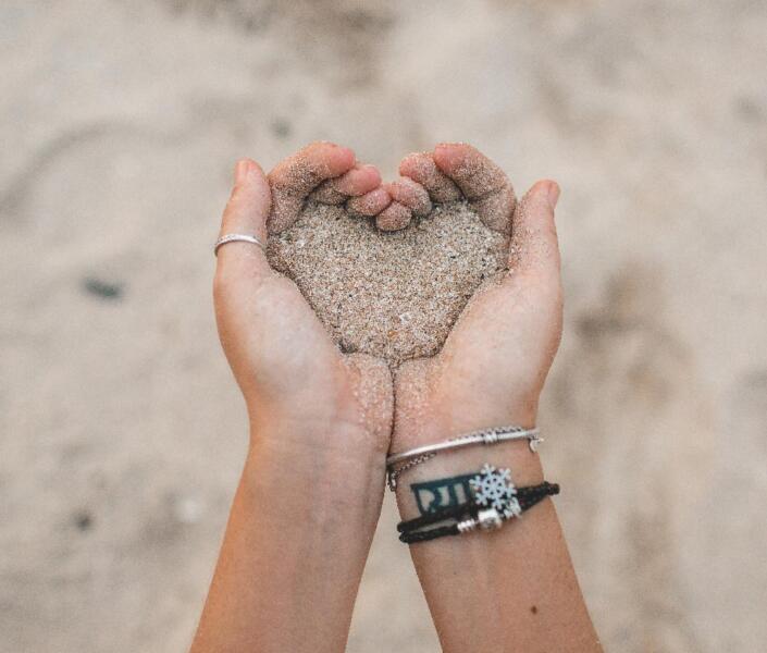 Hands making heart shape and holding sand